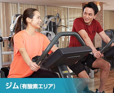 ジム(有酸素エリア)。フィットネスバイクで運動する男女の画像